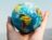 Hand holding a globe against a mountain background symbolizing travel and exploration.