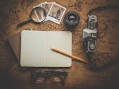 A flat lay of travel essentials on a vintage map surface, including a camera, notebook, and magnifying glass.