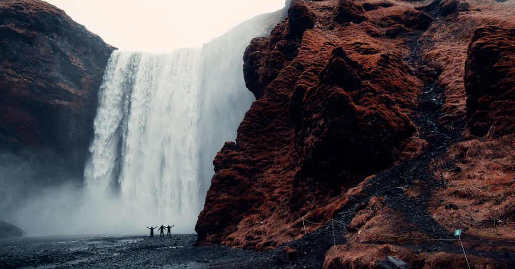 A group of adventurers stands before the majestic Skogafoss waterfall in Iceland.